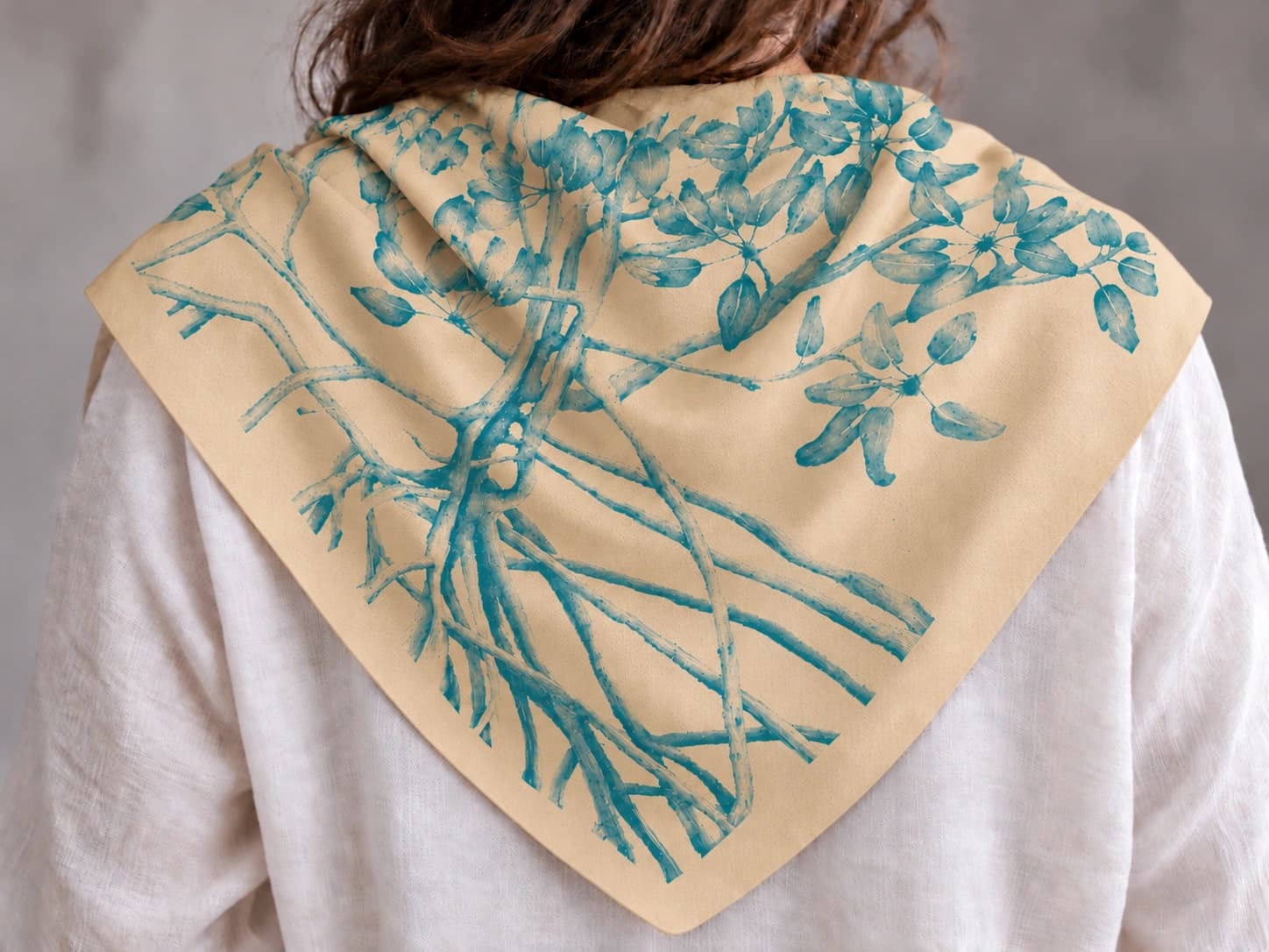 Teal mangrove artwork printed on a buff fabric bandana with a plain unprinted border, draped over shoulders and viewed from behind